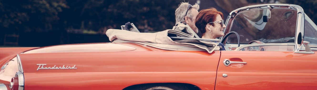 Mature couple driving in a red convertible car.